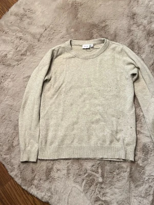 Beige stickad tröja med rund hals - En enkel och stilren beige stickad tröja med rund halsringning och ribbade muddar vid ärmslut och nederkant. Perfekt basplagg att matcha till olika outfits. Tröjan har en mjuk och skön känsla och passar till många tillfällen.