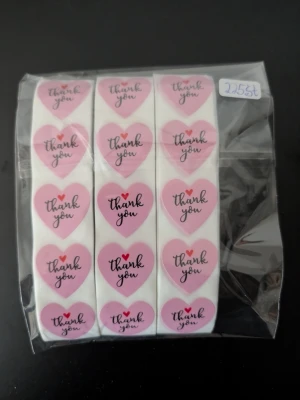 Rullar med rosa hjärtformade klistermärken 225 st - Säljer flera rullar med klistermärken i form av rosa hjärtan med texten 'thank you' i svart och rött. Perfekta för att dekorera paket, brev eller presenter. Kommer i en genomskinlig plastförpackning.