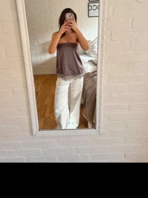 Lila tubtopp med spetskant - Säljer en lila tubtopp i satinliknande material med bred spetskant längst ner. Toppen är axelbandslös och har en avslappnad passform, perfekt för en trendig och enkel look. Passar snyggt till både jeans och kjol.