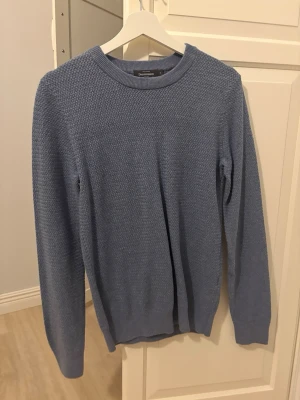 Blå stickad tröja från Dressmann - Säljer en stilren blå stickad tröja från Dressmann i storlek S. Tröjan har rund halsringning, lång ärm och ett diskret strukturmönster i stickningen. Perfekt för lager på lager och enkel att matcha med jeans eller chinos.