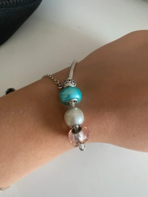 Tre berlocker i glas och metall - Säljer tre snygga berlocker till armband. En är turkosblå och glansig, en är pärlvit och en är ljusrosa och facetterad. Alla har metallkärna och passar till ormkedja. Perfekt för att mixa och matcha till ditt smycke. Vet ej märke eller material