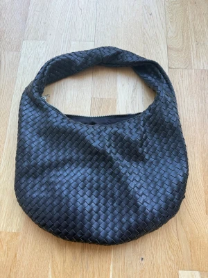 Svart flätad axelväska - Snygg svart axelväska med rundad form och flätad design. Väldigt rymlig. Inte använd super mycket så skulle säga att den är i nytt skick💕