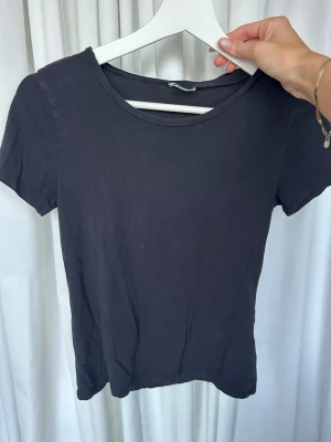 Svart basic t-shirt i bomull - Enkel svart t-shirt i mjuk bomull med rund halsringning och korta ärmar. Perfekt att matcha med jeans eller kjol för en clean och stilren look.