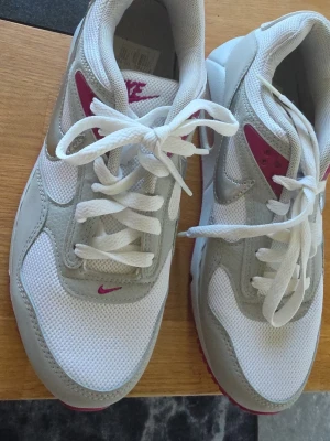 Nike vita och grå sneakers stl.39  - Nike sneakers i vitt och ljusgrått med detaljer i vinrött. Klassisk låg modell med mesh och syntetmaterial, snörning framtill och tydlig Nike-logga på plös och häl. Snygg retrostil som passar till många outfits.