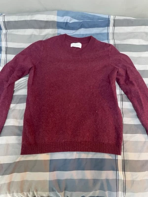 Samsöe stickad ull tröja  - Mysig vinröd stickad tröja med rund halsringning och ribbade muddar. Tröjan är tillverkad i en mjuk ullmix och har en enkel, klassisk design som passar perfekt till höst och vinter.