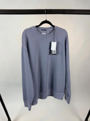 C.P. Comapny crewneck  - En stilren ljuslila sweatshirt med rund hals och avslappnad passform. Tillverkad i mjuk bomull med ribbade muddar vid ärmslut och nederkant. Perfekt för en chill och trendig look.