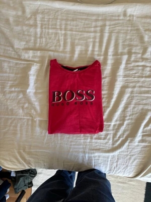 Röd BOSS t-shirt med logga - Snygg röd t-shirt från Hugo Boss med stor BOSS-logga framtill. Klassisk passform och rund halsringning. Perfekt för dig som vill ha en enkel men ändå statement t-shirt. Tillverkad i mjuk bomull för skön känsla hela dagen.