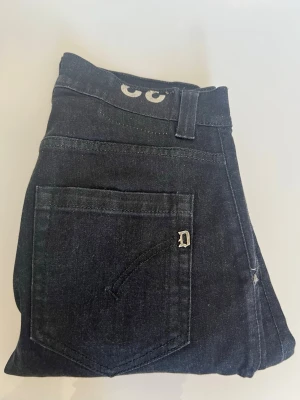 Svarta dondup jeans - Snygga svarta dondup  jeans i slim fit-modell med en liten metallbokstav på bakfickan och coola ögon-detaljer på insidan av linningen. Jeansen har klassisk femficksdesign och raka ben. Perfekta för dig som vill ha en stilren men unik look.w w32 l32