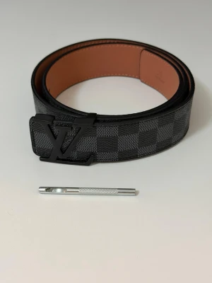 Svart bälte - Snyggt bälte i svart och grått med rutigt mönster. Bältet har en insida i brunt skinn och klassisk design som passar till många olika outfits.