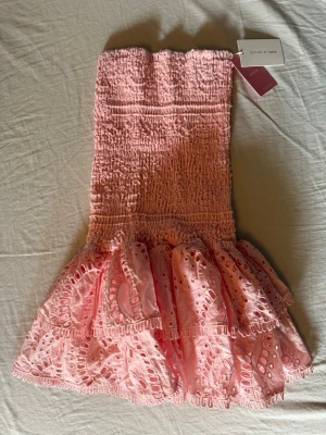 Rosa volangklänning från Design by Amor - Supersöt rosa klänning från Design by Amor med smockad midja och broderade volanger. Aldrig använt
