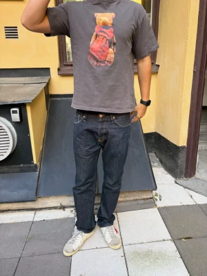 Grå t-shirt med björntryck - Säljer en grå t-shirt med ett stort tryck av en nallebjörn med röd halsduk på bröstet. T-shirten har normal passform och korta ärmar. Perfekt för dig som gillar unika och lekfulla motiv. Materialet känns som bomull.