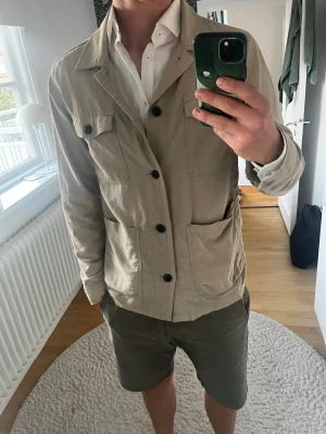 Beige overshirt från Lindbergh - Stilren beige overshirt från Lindbergh med fyra stora fickor framtill och knäppning med svarta knappar. Jackan har klassisk krage och är tillverkad i bomull, perfekt för lager på lager under vår och höst.