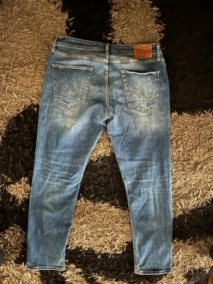 Blå jeans från Jack & Jones - Snygga blå jeans från Jack & Jones med klassisk femficksdesign och raka ben. Jeansen har en ljus tvätt med slitningar och kontrastsömmar. Tillverkade i denim med skinnpatch bak i midjan. Perfekta för en avslappnad och trendig stil.