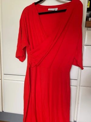 Masai omlottklänning Ny! stl XL - Säljer en röd omlottklänning från Masai i storlek XL. Klänningen har trekvartsärm och en snygg v-ringning framtill. Tillverkad i mjukt och stretchigt material, perfekt för dig som gillar en bekväm och stilren look. Ny och ej använd.