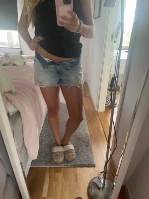 Lågmidjade ljusblå jeansshorts - Säljer ett par lågmidjade ljusblå jeansshorts med slitna detaljer och fransig kant. Shortsen har klassisk femficksdesign och är perfekta för sommaren. Snygg och avslappnad stil som passar till allt.