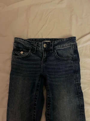 Mörkblå bootcut jeans - Säljer ett par mörkblå bootcut jeans med klassisk femficksdesign och snygga slitningar. Jeansen har hög midja och breda ben, perfekta för en avslappnad och trendig look. Materialet är mjukt denim som sitter skönt hela dagen.