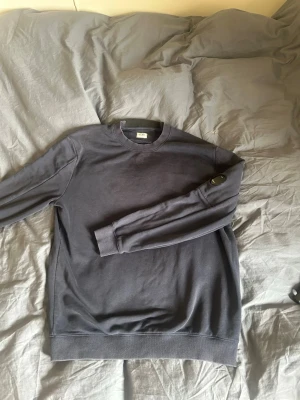 Cp company hoodie - Säljer en mörkgrå sweatshirt från C.P. Company med deras ikoniska linsdetalj på ärmen. Tröjan har rund halsringning, långa ärmar och ribbade muddar. Perfekt för dig som gillar streetwear och vill ha något stilrent men ändå unikt.