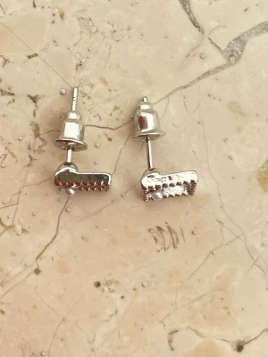 Silvriga fyrkantiga örhängen med pärla - Ett par stilrena örhängen i silverfärgad metall med öppen fyrkantig form. Varje örhänge har en liten pärldetalj i ena hörnet och en kant med små dekorativa detaljer. Perfekta för dig som gillar minimalistisk men ändå unik design. Helt nya aldrig använda.