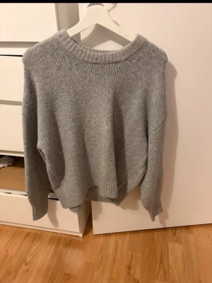Grå stickad tröja - Mysig grå stickad tröja med  bred ribbad krage. Tröjan har långa ärmar och ribbade muddar vid ärmslut och nederkant.  