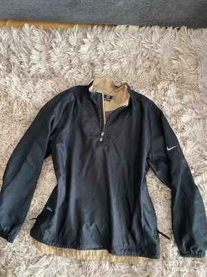 Svart vintage Nike golf jacka - strl L - Svart snygg vintage Nike golf jacka med beige insida. Jackan har lång ärm, halv dragkedja framtill och liten Nike-logga på ärmen. Perfekt för golf eller annan träning eller till vardags. Den har en sportig look med justerbar nederkant.