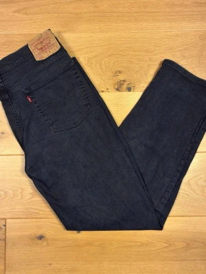  Levi’s 512  W35 L30 - Ett par snygga Levi’s 512 W35 L30 i mörkt, urtvättat svart denim med den karaktäristiska charcoal-tonen som bara äkta Levi’s får med tiden. Slim taper-passform – smalare mot vristen men skön i låret, sitter perfekt både uppsynat och avslappnat.  Detaljer:  * Klassisk femficksmodell * Läderslapp i äkta läder på midjan (Levi Strauss & Co.) * Rött Levi’s-tag på bakfickan * Kopparnitar och Levi’s-knapp i midjan * Rak, slitstark söm som genomgående  Skick: Använda men i fint skick – ingen dokumentera