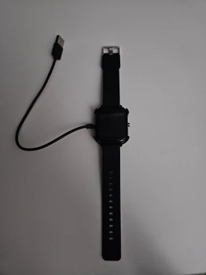 Svart smartklocka med silikonarmband - En stilren svart smartklocka med rektangulär display och justerbart silikonarmband. Klockan har en knapp på sidan och levereras med en USB-laddningskabel. Perfekt för dig som vill ha koll på notiser och aktivitet direkt på handleden.  Fungerar exakt som den ska. Priset kan diskuteras.