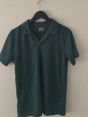 Mörkgrön kortärmad polotopp - En stilren mörkgrön polotopp med korta ärmar och klassisk krage. Tillverkad i ett mjukt och lätt material som känns skönt mot huden. Perfekt för en avslappnad men ändå snygg look.