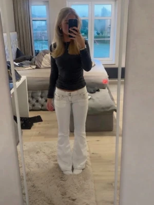 Vita utsvängda jeans med detaljer - Säljer ett par vita jeans med utsvängda ben och låg midja. Jeansen har dekorativa sömmar och fickor både fram och bak. Perfekta för dig som gillar en trendig och retro look. Materialet ser ut att vara klassisk denim med stretch.