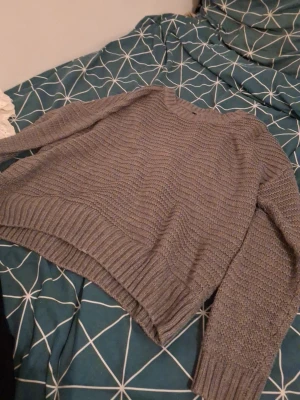 Grå stickad tröja med strukturmönster - Mysig grå stickad tröja med rund hals och lång ärm. Tröjan har ett snyggt strukturmönster och breda ribbade muddar vid ärmslut och nederkant. Perfekt för kyliga dagar och enkel att matcha med jeans eller kjol.