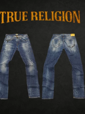 True Religion ROCCO Relaxed Skinny W32 blå jeans - ❌ Passformsbilder skickas ej. Se mått! Säljer ett par blå jeans från True Religion med slitningar och tvättade detaljer. Klassisk femficksmodell med raka ben och låg midja. Snygga kontrastsömmar och patch bak på linningen. Perfekta för en avslappnad och trendig look.Det finns en mörk fläck på höger framficka och bakficka. Fläckarna är inte behandlade och har inte gått igenom tyget.💬 Prisförslag välkomnas. 🚫 Rökfritt & djurfritt hem. 📦 Skickas inom 24 timmar. 😱 Smutsfläckar kan förekomma