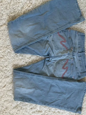Ljusblå bootcut jeans från Nelly  - Ett par ljusblå bootcut jeans med snygga broderade detaljer i rött på bakfickorna. Jeansen har klassisk femficksmodell. Perfekta för en avslappnad och trendig look. Bara använda några enstaka gånger och har inga slitningar. Storlek 34 🩷