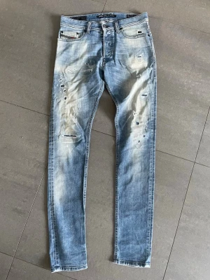 Diesel jeans - Säljer ett par ljusblå slim fit jeans från Diesel, modell Tepphar. Jeansen har stretch, slitningar och hål på både fram- och baksida för en trendig look. Perfekta för dig som gillar en avslappnad och modern stil.