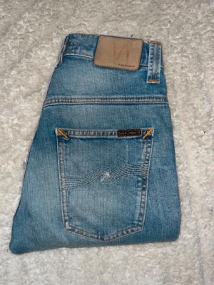Nudie jeans  - Ljusblåa jeans från Nudie Jeans i modellen Tape Ted. Midja 32cm, längd 105cm. JAG SKICKAR EJ FLER BILDER NÄR JAG BÄR JEANSEN! för bättre inblick i passformen rekommenderar jag att googla på modellnamnet. För storleksguide kolla måtten noggrant då jeansen alltid kan vara uppsydda heller krympta och jag ej tar emot returer :) (n5)