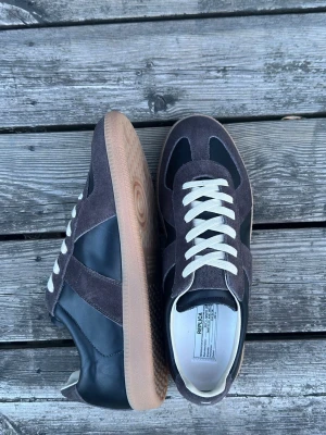 Maison Margiela Gats - Säljer ett par maison margiela gats i en brun svart colourway. Nästan helt nya och alla tillbehör så som box och dustbags medföljer✅ Frågor? Kontakta mig ✅ storlek 45 passar 44 (box har en liten deffekt)