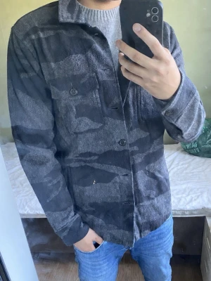 Overshirt camo från abercrombie&fich - Snygg grå overshirt med svart camomönster och knäppning framtill. Skjortan har två bröstfickor med lock och knappar samt klassisk krage. Perfekt lager-på-lager-plagg för en avslappnad stil.
