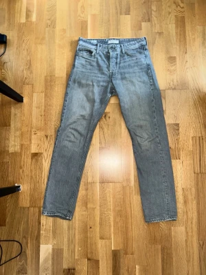 Grå loose fit jeans från Jack & Jones - Säljer ett par grå loose fit jeans från Jack & Jones, modell Chris. Jeansen har klassisk femficksdesign, raka ben och knappgylf. Materialet är tvättad bomull med en lätt sliten look. Perfekta för en avslappnad stil.