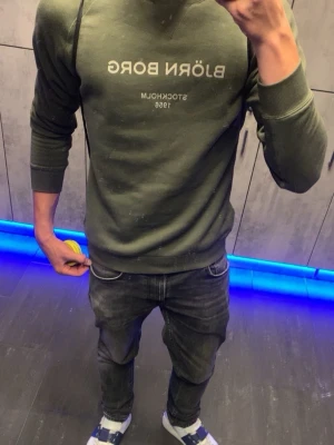 Olivgrön sweatshirt från Björn Borg - Olivgrön sweatshirt från Björn Borg med tryckt logga och texten 'STOCKHOLM 1956' på bröstet. Tröjan har rund halsringning, ribbade muddar vid ärmslut och nederkant samt en avslappnad passform. Perfekt för en casual look. knappt använd häller så riktigt go och ny