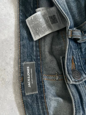 Blå jeans från Jack & Jones - Säljer ett par klassiska blå jeans från Jack & Jones. Jeansen har raka ben, fem fickor och snygga kontrastsömmar. Tillverkade i slitstarkt denim med en tidlös tvätt. Perfekta för en avslappnad och trendig look.