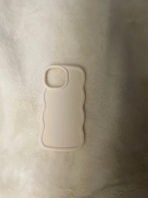 Beige vågigt mobilskal  iPhone 13 Pro Max - Snyggt beige mobilskal med vågig kantdesign. Tillverkat i mjukt silikon som ger ett bra grepp och skyddar mobilen mot repor. Är i storlek iPhone 13 Pro Max.