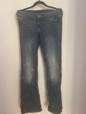 Blå bootcut jeans med slitningar - Säljer ett par blå bootcut jeans med snygga slitningar och tvättade detaljer. Jeansen har klassisk femficksmodell, normal midja och dragkedja med knapp. Perfekta för en avslappnad och trendig look.