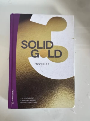 Solid Gold 3 Engelska 7 kursbok - Solid Gold 3 är en kursbok för Engelska 7 på gymnasiet. Boken har ett hårt omslag i vitt, guld och lila med tydlig text och modern design. Författare är Eva Hedencrona, Karin Smed-Gerdin och Peter Watcyn-Jones. Utgiven av Studentlitteratur.