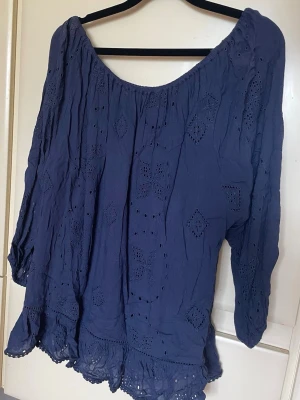 Fiore blus blå med broderade detaljer stl L - Säljer en blå blus med broderade hålmönster och rund halsringning. Blusen har korta ärmar och en lätt volang nertill. Perfekt för dig som gillar en luftig och söt stil.