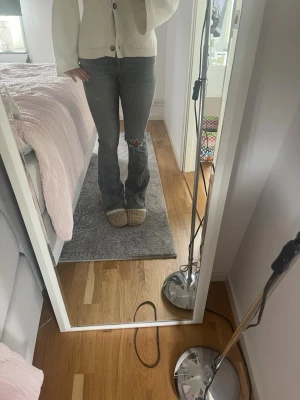 Grå bootcut jeans med slitning - Säljer ett par grå bootcut jeans med slitning och hål på ena knät. Jeansen har en klassisk femficksmodell och är tillverkade i denim med lätt stretch. Perfekta för dig som gillar en avslappnad och trendig stil.