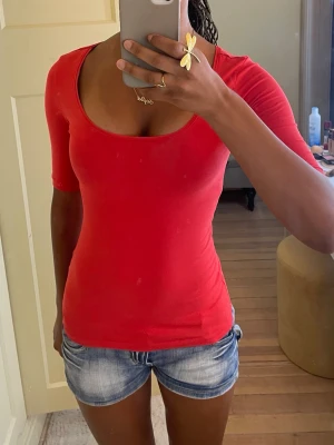 Röd topp med rund ringning - En enkel och snygg röd topp med rund, djup ringning och halvlånga ärmar. Modellen är figurnära och passar perfekt till jeans eller kjol. Tillverkad i mjukt bomullsmaterial som känns skönt mot huden.