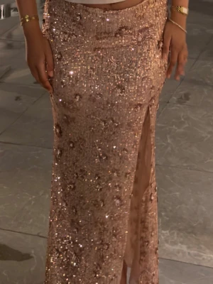 Oh Polly glitter kjol - Säljer en glittrig långkjol i guld med paljetter och en snygg slits framtill. Kjolen har en figurnära passform och är perfekt för dig som vill sticka ut. Materialet är syntet och kjolen har en elegant och festlig känsla.