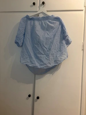 Ljusblå offshoulder blus - Söt ljusblå offshoulder blus med resår upptill och trekvartsärm. Tillverkad i ett tunt och luftigt tyg som passar perfekt till sommaren. Blusen har en avslappnad passform och är lätt att styla med jeans eller kjol.