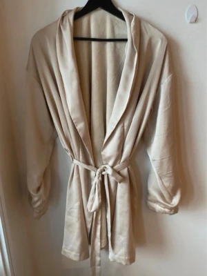 Beige satängkimono från Lindex, storlek M - Super fin beige satängkimono från Lindex i storlek M, den har ett mjukt fluff på insidan