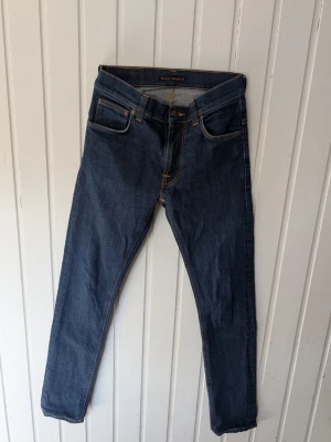 Mörkblå jeans från Nudie Jeans - Snygga mörkblå jeans från Nudie Jeans med klassisk femficksmodell och kontrastsömmar. Jeansen har rak passform och är tillverkade i slitstark denim. Perfekta för dig som gillar stilrena och tidlösa jeans.