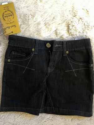 Lågmidjad jeanskjol - Lågmidjad svart jeans kjol med superfina detaljer. Materialet känns lyxigt och tillkommer även en extra metallknapp. Helt oanvända, lappen kvar. 