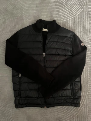 Svart cardigan jacka Moncler - Svart cardigan jacka mer moncler märke på vänstra ärmen. Tvär najs jacka som jag använt mycket men tagit hand om väl. Den har lite slitage på vänstra ärmens änd men det märks knappt om man inte kollar just där. Själva ”handtagen” på drag kedjorna har börjat blivit lite missfärgade men inget som man tänker på. Tyget är smått solblekt men inget som man tänker på! Allmänt skön jacka och den har varit en av mina favoriter men den börjar bli för liten och därför ska den nu bort. 